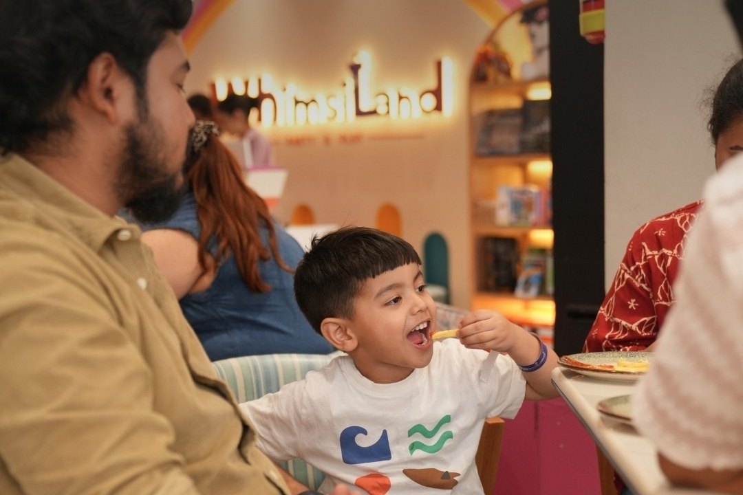 A boy laughing over lunch at Wizzy Café, the WhimsiLand rainbow behind him