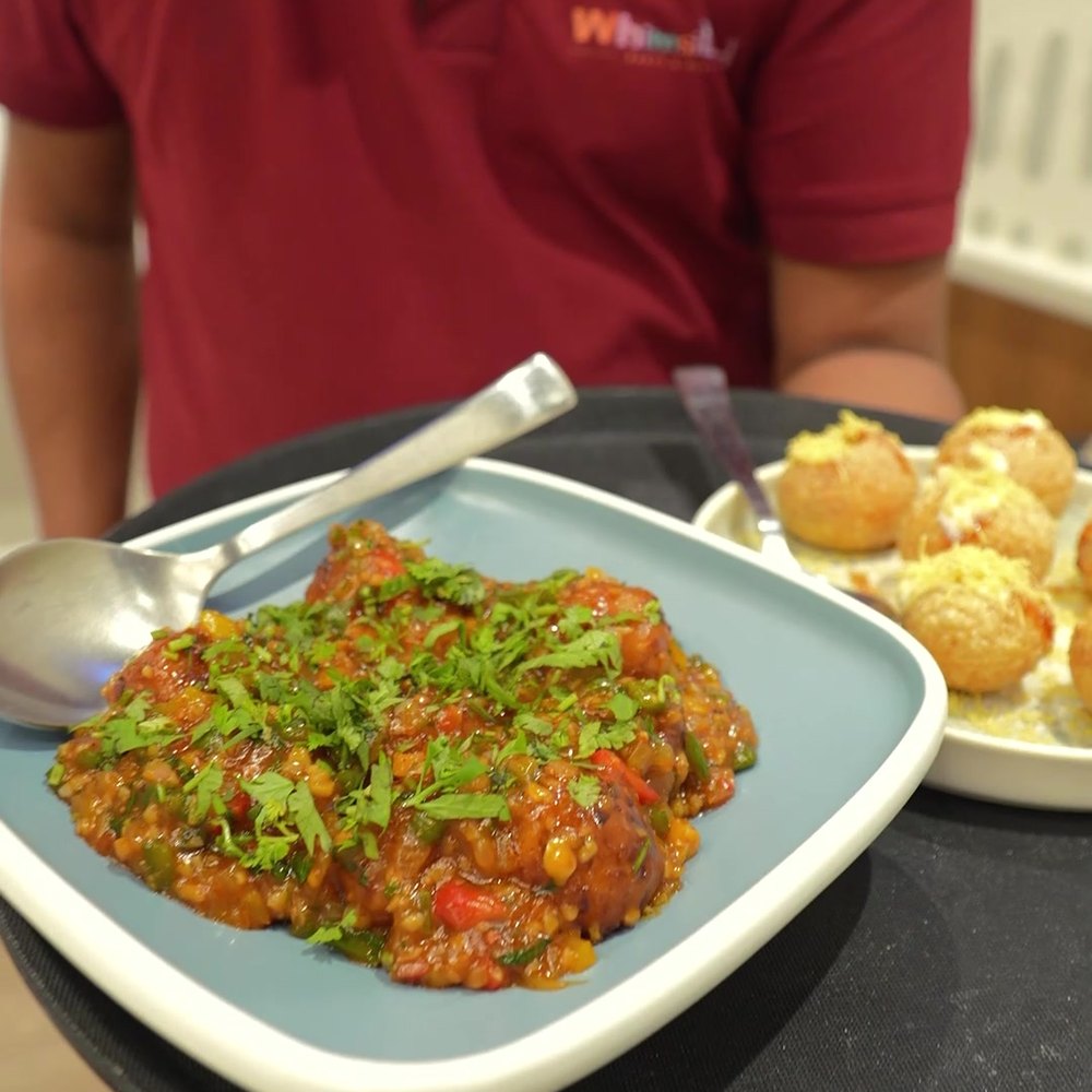A freshly plated dish being carried to a table at Wizzy Café
