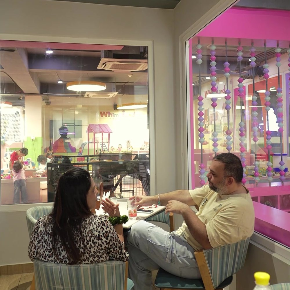 Parents at a table with the play area visible through the glass behind them
