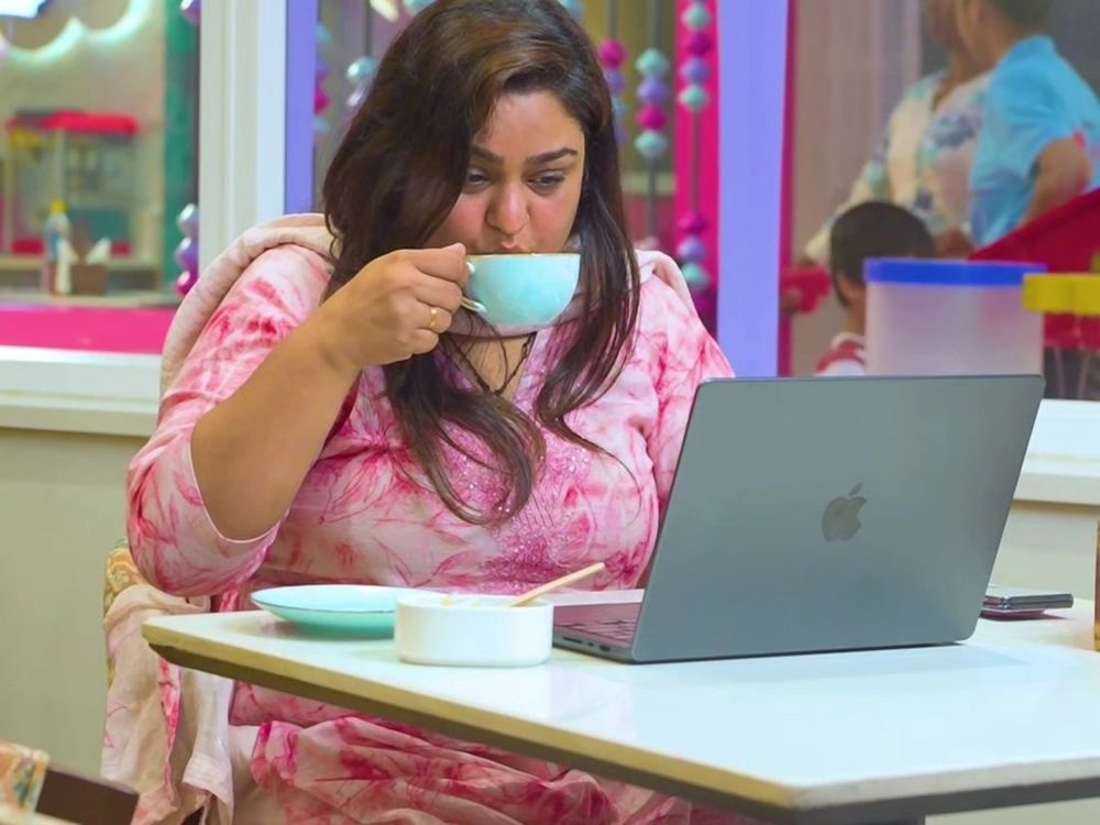 A parent drinking coffee at a laptop while children play behind the glass