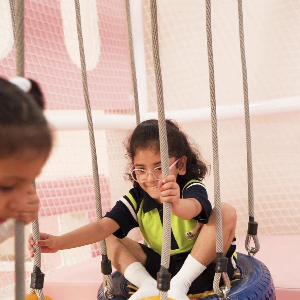 Two children in school uniform on the tyre swings over the foam pit